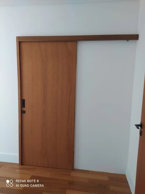 Porta de correr de madeira com trilho superior coberto, em ambiente com piso amadeirado.