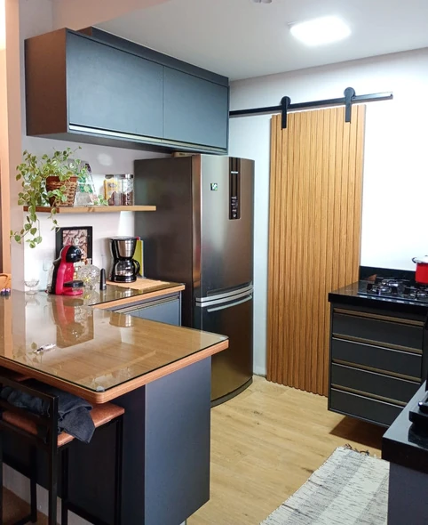 Cozinha com armários cinza, bancada amadeirada e geladeira ao lado de porta de correr ripada.