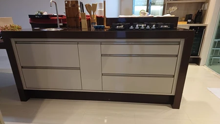 Ilha de cozinha com gavetas claras, estrutura escura e cooktop sobre a bancada.