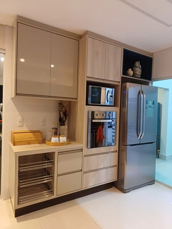 Armários de cozinha com forno e micro-ondas embutidos, cestos metálicos e geladeira ao lado.