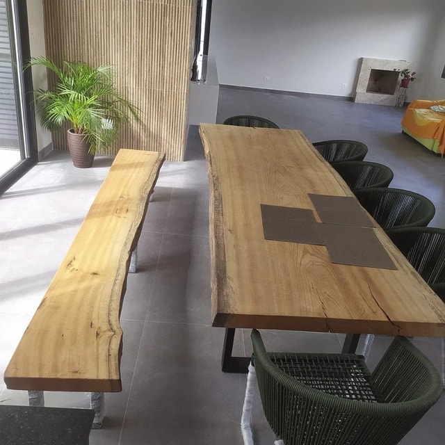 Mesa de aparência amadeirada vista de cima, banco à esquerda e cadeiras verdes à direita.