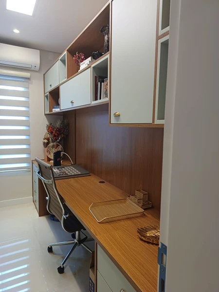 Escritório estreito com bancada amadeirada, cadeira giratória e armários verde-claro com puxadores dourados.