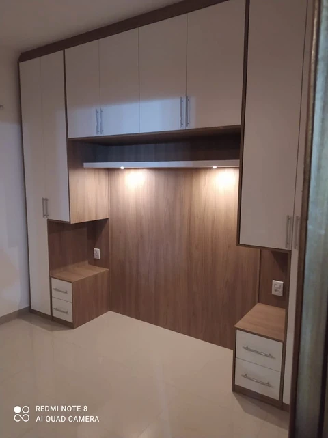 Marcenaria de quarto com armários claros ao redor de painel amadeirado e gaveteiros laterais.